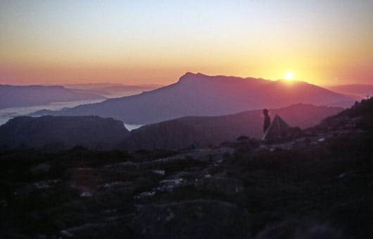 tas-anne_dawn Tasmania, and the unspeakable beauty of the high mountains. As the morning's sun rises over the long ridge of Mt Weld, a hiker emerges from their tent high on the summit plateau of Mt Anne. At this hour there is plenty of time to eat breakfast and contemplate the mountain grandeur as hands are warmed by a steaming cup of strong tea.