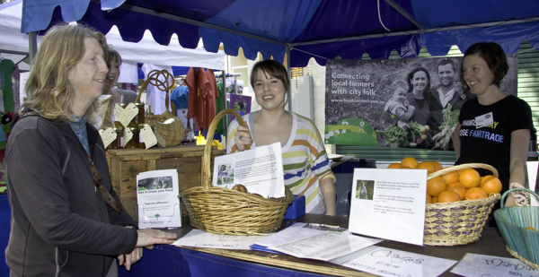 Buyers and sellers talk about food at a CSA stand at a market. CSA’s are a type of social enterprise food distribution scheme.